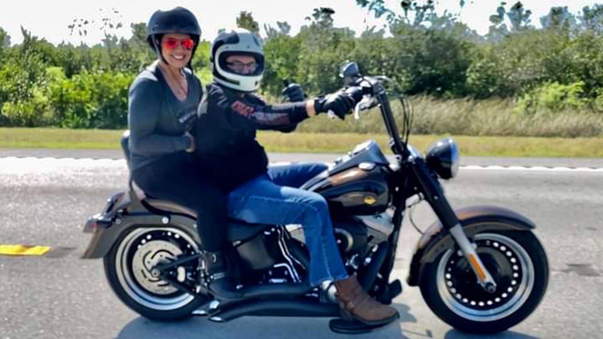 Alex and his wife wearing helmets while smiling for a picture and riding on Alex’s motorcycle. 