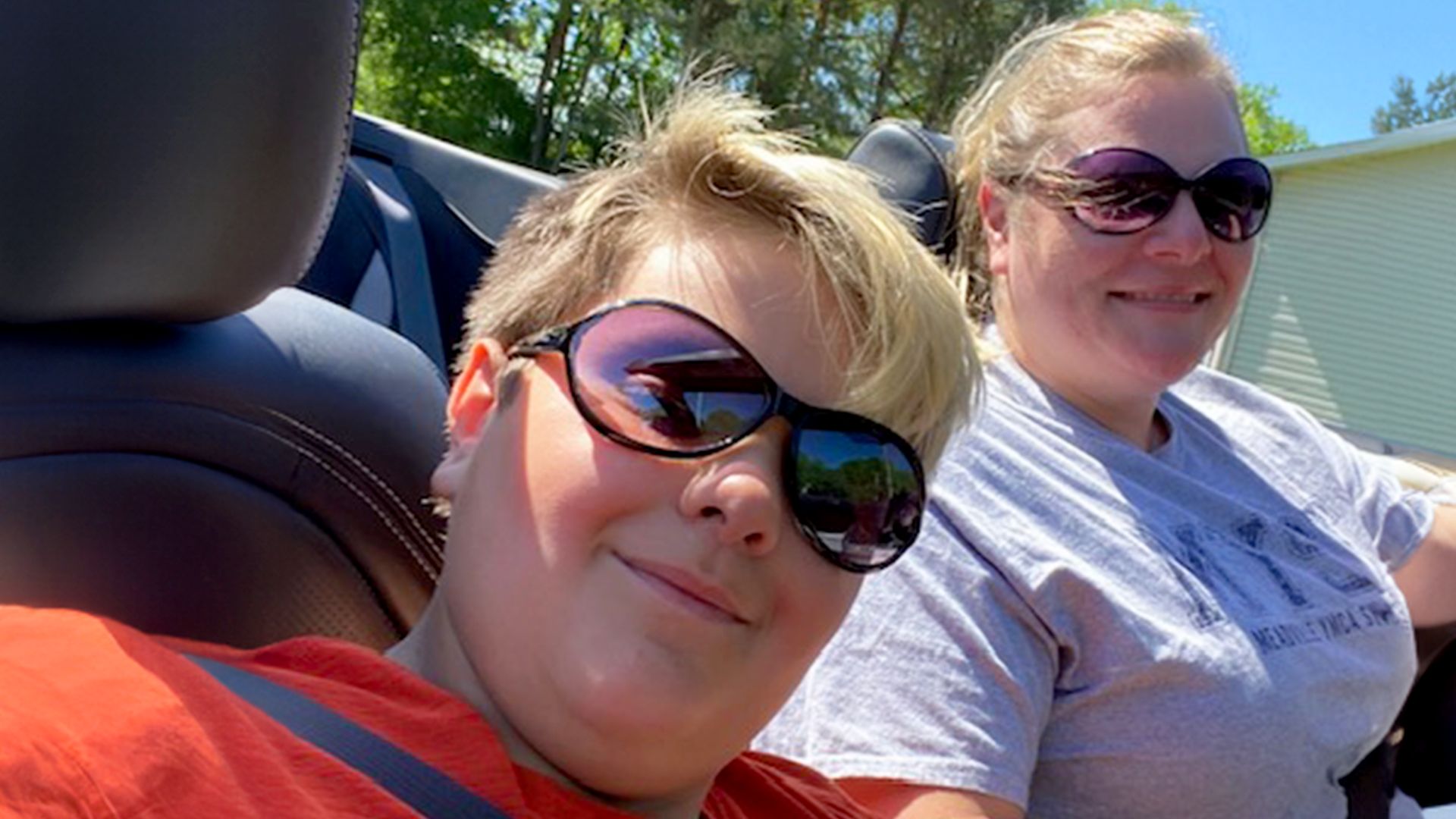 Alicia and Landon smiling while wearing sunglasses and riding along in Alicia’s convertible.